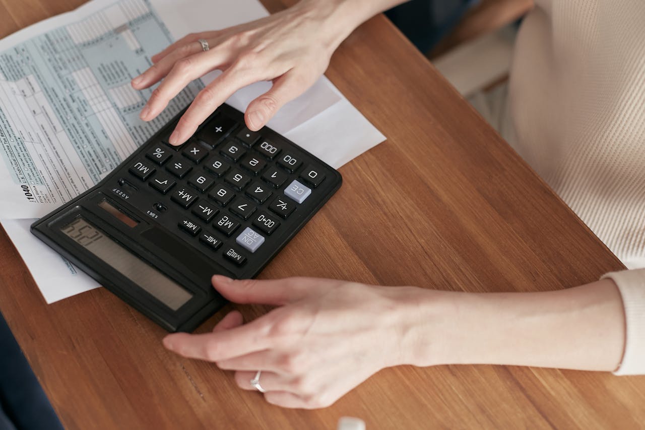 heros-img Close-up of a woman using a calculator and reviewing bills at home.